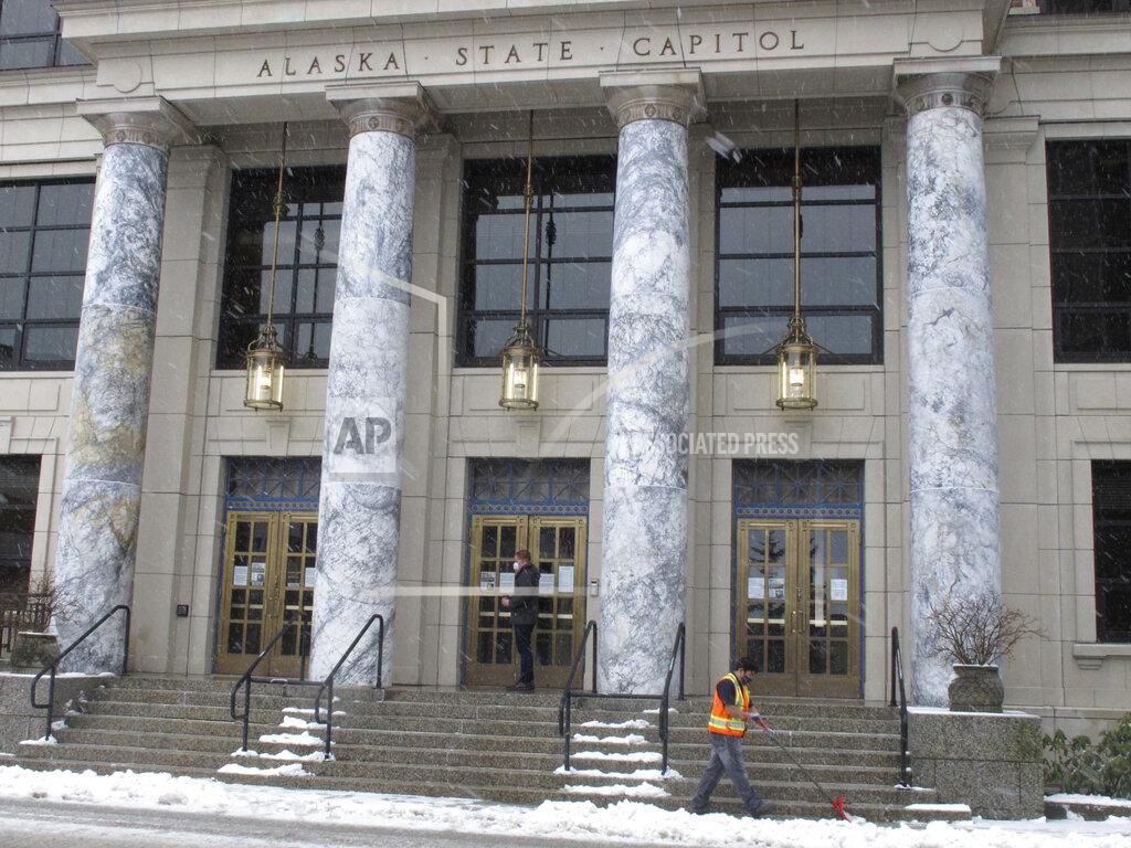 A legislative aide enters the Alaska State Capitol as a worker clears snow from in front of the building on Thursday, Feb. 25, 2021, in Juneau, Alaska. The Alaska House speaker announced on Wednesday, Feb. 24, that a House member had tested positive for COVID-19. (AP Photo/Becky Bohrer)