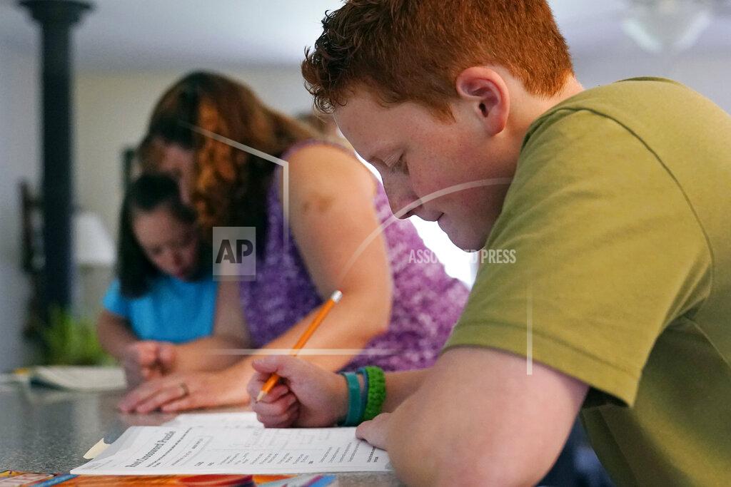 Charles Krupa Noah Osgood, 12, right, works on a review sheet as his mother, Jennifer, helps his sister, Lily, at their home in Fairfax, Vt., on Tuesday, July 20, 2021. “He told me he was learning so much more at home than he ever did in school,’’ Jennifer says. “He said, ‘School is just so chaotic -- we don’t get very much done in any particular class. Here, I sit down, you tell me what to do, and minutes later I’m done.'” (AP Photo/Charles Krupa)
