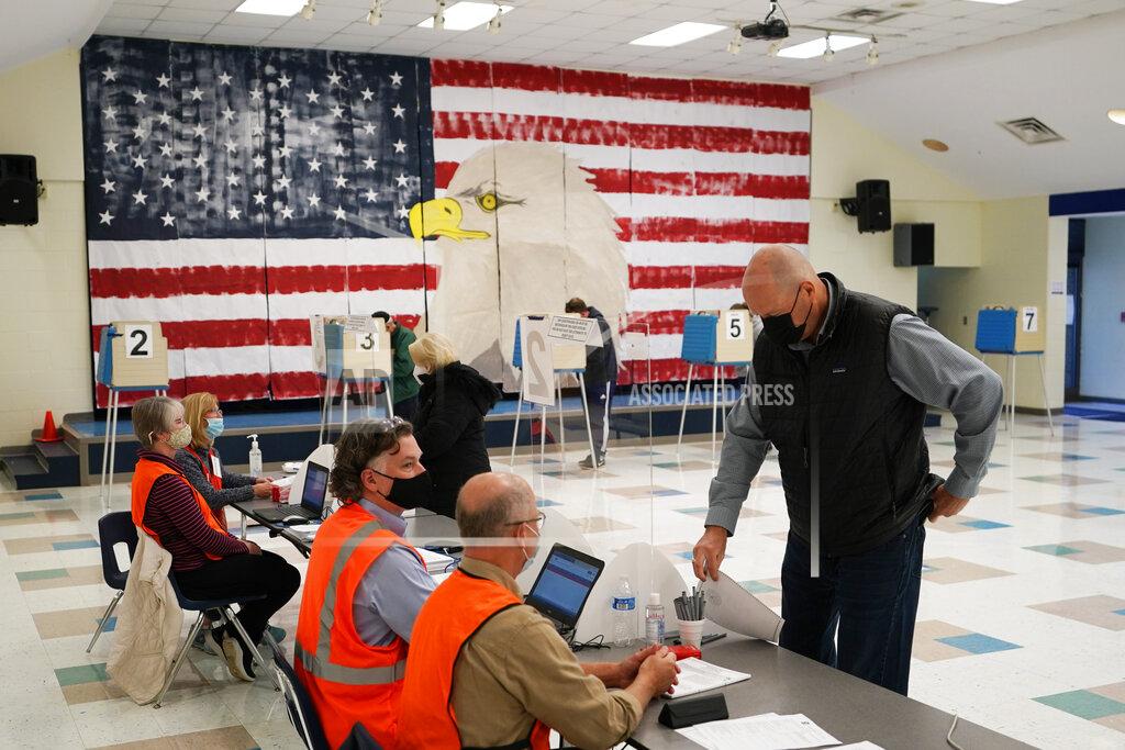 Steve Helber CORRECTS MONTH TO NOVEMBER A voter check with the registration table as he prepares to cast his ballots under a giant mural at Robious Elementary school on Election Day, in Midlothian, Va., Tuesday Nov. 3, 2020. Poll workers said that traffic was slow due to all the early voting in the precinct. (AP Photo/Steve Helber)