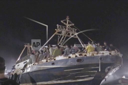 In this frame taken from video, a fishing boat with migrants is docked at the port of the Sicilian island of Lampedusa, southern Italy, late Monday, Sept. 27, 2021. A rusty, overloaded fishing boat carrying nearly 700 migrants arrived at an Italian island port amid fresh diplomatic efforts by Mediterranean governments to seek more European help in handling migrant flows. (AP Photo/Mauro Buccarello)