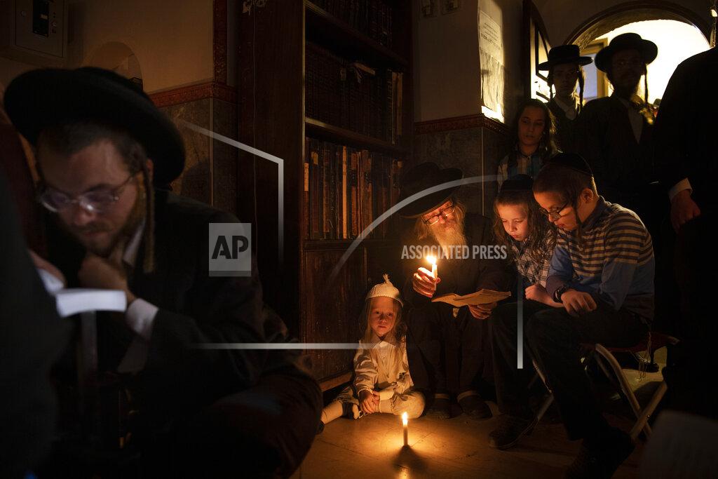Oded Balilty Ultra-Orthodox Jewish men and children read by candle light from the book of Eicha (Book of Lamentations) during the annual Tisha B'Av (Ninth of Av) fasting and a memorial day, commemorating the destruction of ancient Jerusalem temples, in the Ultra-Orthodox neighborhood of Mea Shearim in Jerusalem, Saturday, July 17, 2021. (AP Photo/Oded Balilty)