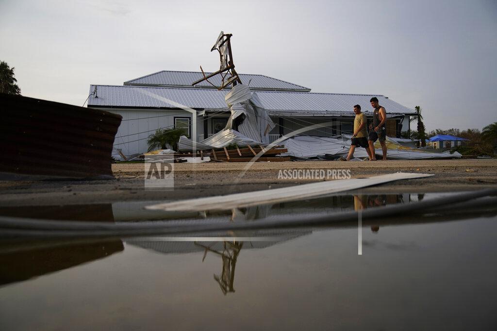 John Locher People walk by buildings damaged by Hurricane Ida, Monday, Sept. 6, 2021, in Grand Isle, La. (AP Photo/John Locher)