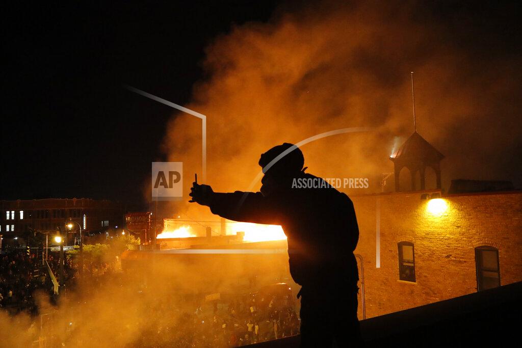 Julio Cortez A man makes a video of protesters from the roof of the Minneapolis police 3rd Precinct building, Thursday, May 28, 2020, in Minneapolis. Protests over the death of George Floyd, a black man who died in police custody Monday, broke out in Minneapolis for a third straight night. (AP Photo/Julio Cortez)