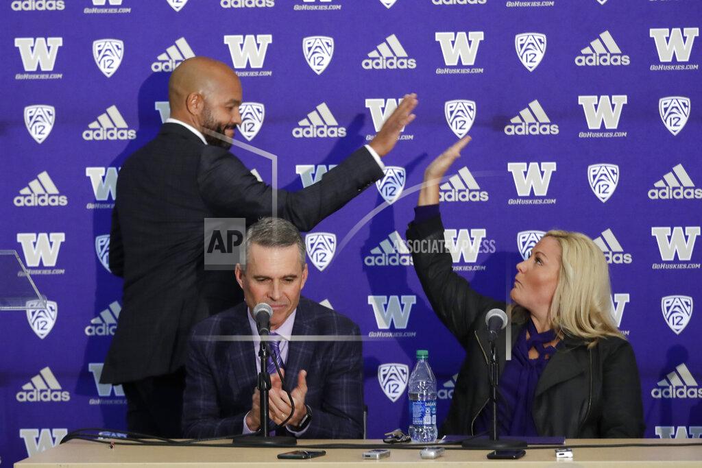 Washington NCAA college football head coach Chris Petersen, center, applauds as defensive coordinator Jimmy Lake, left, high-fives athletic director Jen Cohen after speaking during a news conference about Petersen's decision to resign and Lake taking over his job, Tuesday, Dec. 3, 2019, in Seattle. Petersen unexpectedly resigned on Monday, a shocking announcement with the Huskies coming off a 7-5 regular season and bound for a sixth straight bowl game under his leadership. Petersen will coach Washington in a bowl game, his final game in charge. (AP Photo/Elaine Thompson)
