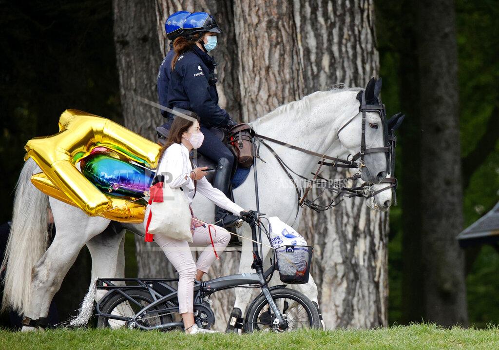 Olivier Matthys Police patrol as a woman rides her bike carrying balloons at the Bois de la Cambre park, during a party called "La Boum 2", in Brussels, Saturday, May 1, 2021. Police put on extra patrols Saturday to monitor the gathering which is being held in defiance of Belgium's current COVID-19 regulations. (AP Photo/Olivier Matthys)