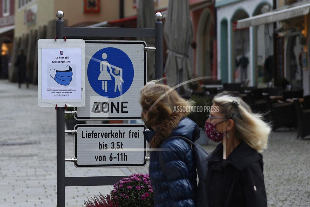 Matthias Schrader People pass a sign reading 'Face masks mandatory from here' in the deserted city of Berchtesgaden, Germany, Monday, Oct. 26, 2020. Authorities have posed the Berchtesgaden region under a lockdown since Oct. 20, 2020 due to a rising number of cases of the pandemic COVID-19 disease caused by the SARS-CoV-2 coronavirus in the district of Berchtesgadener Land. Local authorities in Bavaria's Rottal-Inn county, on the border with Austria, said Monday that the restrictions will begin at midnight. (AP Photo/Matthias Schrader)