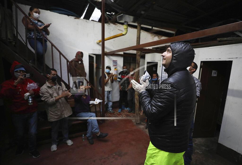 Fernando Vergara FILE - In this March 30, 2020 file photo, Emiliano Moscoso, right, talks to Venezuelan and Colombian people in a boarding house in Bogota, Colombia. Moscoso recently launched a program called Solidarity Menu to feed people in need during the coronavirus outbreak. (AP Photo/Fernando Vergara, File)