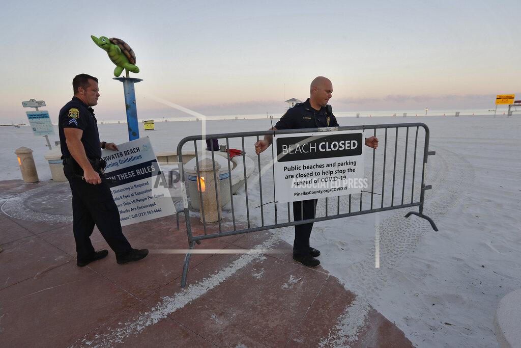 Chris O'meara Clearwater police officers Cpl. Jarred Stiff, left, and Lt. Nate Burnside remove the baracades to officially reopen Clearwater Beach to the public Monday, May 4, 2020, in Clearwater Beach, Fla. Many public beaches and restaurants are reopening as part of Florida Gov. Ron DeSantis' phase one to stop the spread of the coronavirus. (AP Photo/Chris O'Meara)
