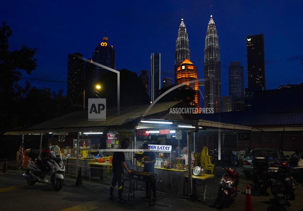 Vincent Thian A local food vendor prepares food with the Twin Towers in downtown Kuala Lumpur in the background background, Malaysia, Monday, Jan. 11, 2021. Prime Minister Muhyiddin Yassin says Malaysia's health care system is at a breaking point as he announced new movement curbs, including near-lockdown in Kuala Lumpur and several high-risk states to rein in a spike in coronavirus cases.(AP Photo/Vincent Thian)