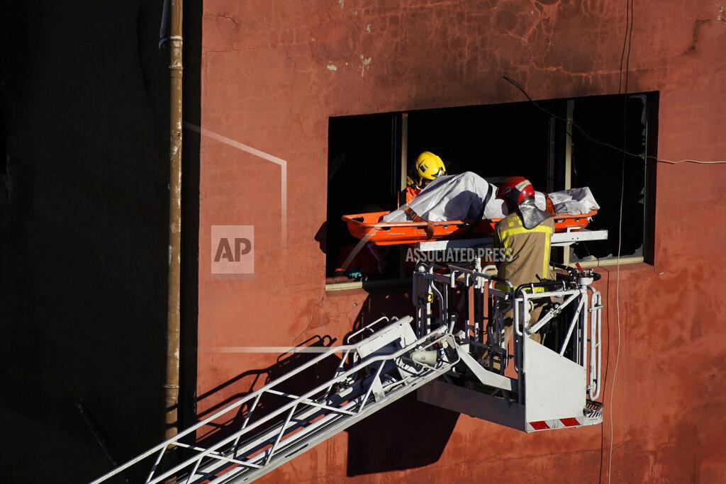 Joan Mateu Firefighters load the body of a dead person into a crane after a fire on a building in Badalona, Barcelona, Spain, Thursday, Dec. 10, 2020. Authorities in northeastern Spain say a fire has raged through an abandoned building occupied by squatters in the city of Badalona, injuring at least 17 people, including two in critical condition. Firefighters say they rescued around 30 people from windows as the building burned late Wednesday. (AP Photo/Joan Mateu)