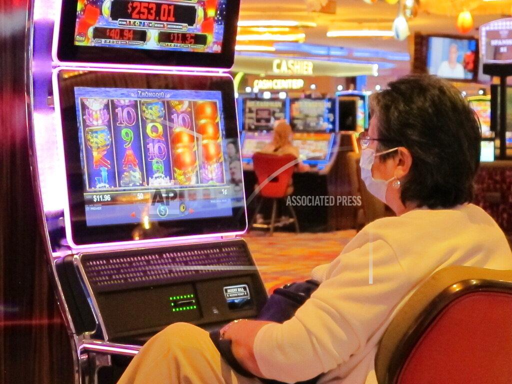 Wayne Parry A gambler wears a mask while playing a slot machine at the Hard Rock casino in Atlantic City, N.J, on July 2, the day it reopened after being closed for 3 1/2 months due to the coronavirus outbreak. Figures released on April 9, 2021, showed Atlantic City's nine casinos collectively saw their gross operating profits decline by more than 80% in 2020 amid the pandemic. (AP Photo/Wayne Parry)