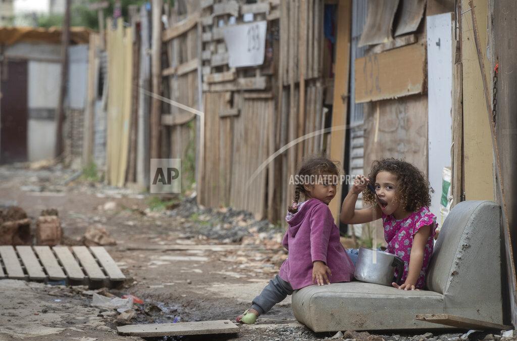 Andre Penner FILE - In this May 15, 2021, a girl eats from a pot as she eyes the camera in the Penha Brasil favela where families have started relocating during the coronavirus pandemic in Sao Paulo, Brazil. The shantytown's rapid rise reflects a resurgence in poverty after the government limited socioeconomic turmoil in 2020 with one of the world's most generous welfare programs. (AP Photo/Andre Penner, File)