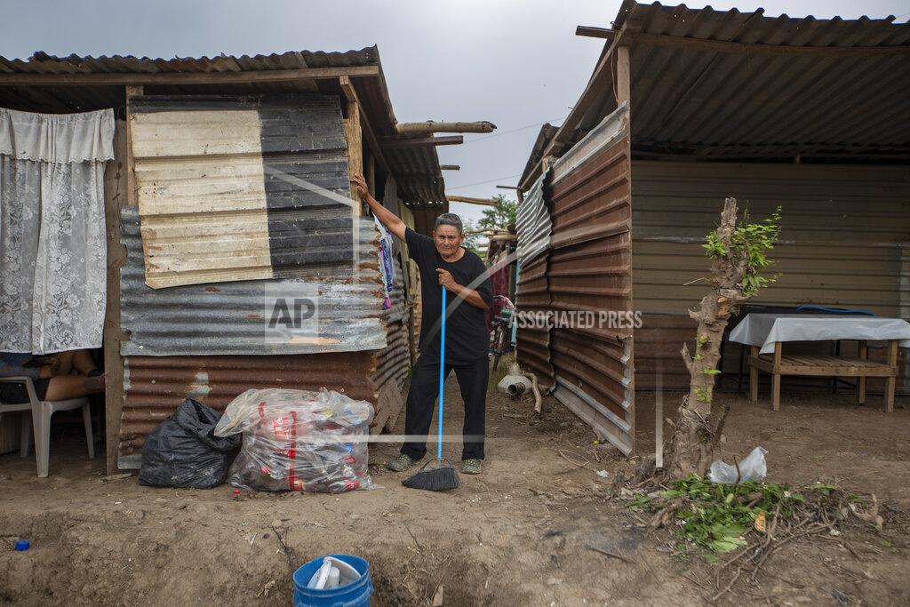 Moises Castillo A neighbor pauses as he cleans outside his shack, built after his home was destroyed by last year's hurricanes Eta and Iota in the La Samaritana community of La Lima, on the outskirts of San Pedro Sula, Honduras, Wednesday, Jan. 13, 2021. La Lima has seen small businesses begin to reopen, but in outlying neighborhoods, the streets are still full of debris, dead animals, snakes and burning mattresses. (AP Photo/Moises Castillo)