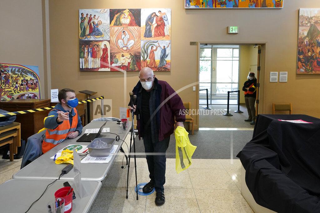 Ted S. Warren Volunteer worker Art Pasette checks in for his shift as a volunteer worker at a mass vaccination clinic at Seattle University, Friday, Feb. 26, 2021, in Seattle. Pasette said he already has been vaccinated for COVID-19, but as states ramp up vaccination distribution in the fight against the coronavirus and volunteers are needed to do everything from direct traffic to check people in to keep vaccination sites running smoothly, volunteer workers are often given a shot in return for their work, — including those who are young and healthy and may not have otherwise been able to receive the shot until later in the year. (AP Photo/Ted S. Warren)
