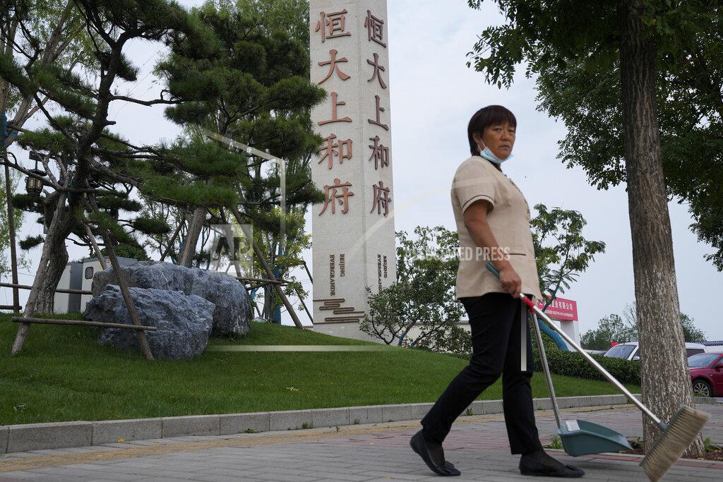 Andy Wong FILE - In this Sept. 15, 2021, file photo, a cleaner walks by the Evergrande's name and logo at its new housing development in Beijing. Global investors are watching nervously as one of China’s biggest real estate developers struggles to avoid defaulting on tens of billions of dollars of debt, fueling fears of possible wider shock waves for the Chinese financial system. Chinese regulators have yet to say what they might do about Evergrande Group. (AP Photo/Andy Wong, File)