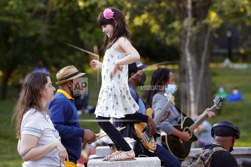 In this Tuesday, June 16, 2020, photo, a young girl dances with her mother to the music of Alegba and Friends, a Haitian jazz and roots band performing nightly free concerts at Prospect Park's landmark boathouse in New York. The band's leader, Alegba Jahyile, who is Haitian, says, "When people come here, they come to have a little good time, to have a picnic with their family, their friends, their lovers. And then the music takes them to another level." Jahyile says he's seen people respond to his music, so he intends to continue the concerts "until the next snowflakes fall." (AP Photo/Kathy Willens)
