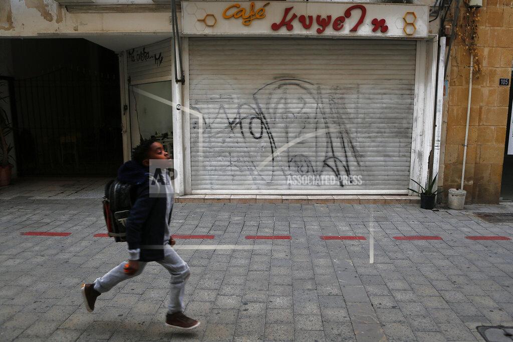 Petros Karadjias A boy runs past a closed cafe in the medieval core of central capital Nicosia, Cyprus, Friday, Dec. 11, 2020. Cyprus' Health Minister Constantinos Ioannou said that an island-wide night time curfew would be extended through December while bars, restaurants and shopping malls would be shut, high school students would stay at home for online classes and church services would be without worshippers amid concerns that a sustained spike in coronavirus infections hasn't receded despite restrictions. (AP Photo/Petros Karadjias)