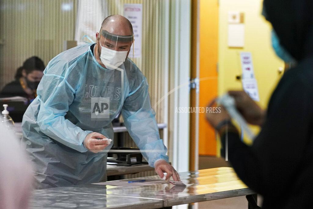 Ted S. Warren Brant McAdams, left, football coach at Pacific Lutheran, wears personal protective equipment as he prepares COVID-19 tests for student athletes Wednesday, Feb. 3, 2021, on campus in Tacoma, Wash. There was never a chapter in any of the books on becoming a small NCAA college football coach that addressed administering COVID-19 tests in the midst of a pandemic, but now it's something he's doing to give his players the chance at a season. (AP Photo/Ted S. Warren)