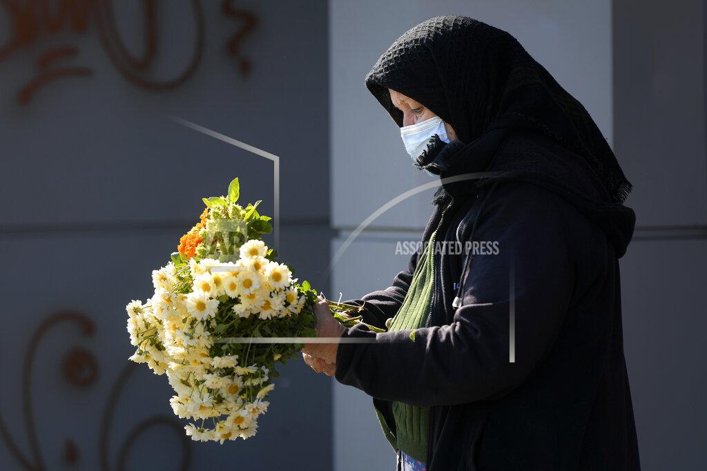 Andreea Alexandru An elderly flower vendor wears a face mask for protection against COVID-19 infection in Bucharest, Tuesday, Oct. 20, 2020. Local authorities imposed the use of face masks in all public spaces, indoors and outdoors, closed schools, restaurants, theatres and cinemas after the rate of COVID-19 infections went above 3 cases per 1000 inhabitants in the Romanian capital Bucharest. (AP Photo/Andreea Alexandru)