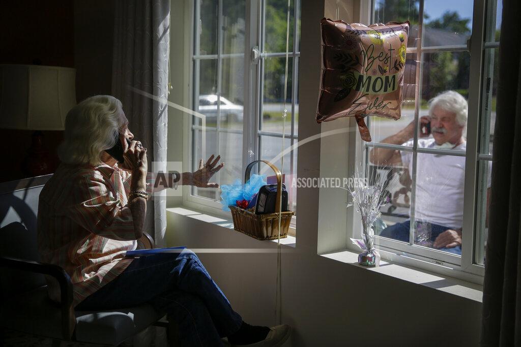 Brynn Anderson FILE - In this Sunday, May 10, 2020 file photo, Mary Faye Cochran, 86, sings "You Are My Sunshine" over the phone to her son Stacey Smith through a window for a Mother's Day celebration at Provident Village at Creekside assisted living facility in Smyrna, Ga. The U.S. has been dramatically disrupted in a matter of months, brought low by a global pandemic, Depression-era economic dislocation, and then, nationwide unrest over racial injustice. (AP Photo/Brynn Anderson)