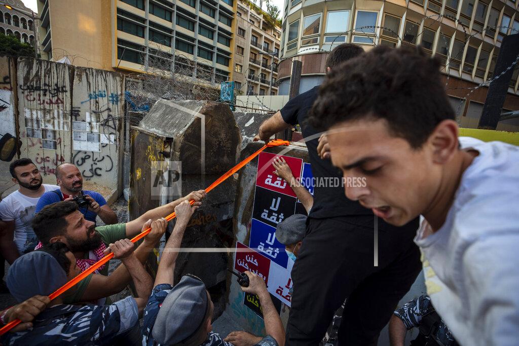 Hassan Ammar Anti-government protesters try to remove a concrete wall that was installed by security forces to prevent them from reaching the government palace in Beirut, Lebanon, Thursday, July 2, 2020. Major retailers in Lebanon announced Thursday they will temporarily close in the face of an increasingly volatile currency market and their inability to set prices while the local currency tumbles before the dollar. (AP Photo/Hassan Ammar)