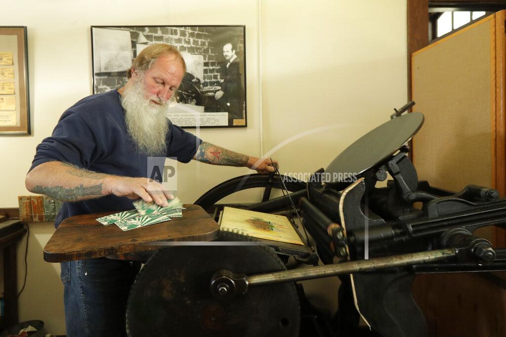 In this May 21, 2020 photo, Loren Ackerman prints wooden money on an 1890s-era press in Tenino, Wash. In an effort to help residents and local merchants alike get through the economic fallout of the coronavirus pandemic, the small town has issued wooden currency for residents to spend at local businesses, decades after it created a similar program during the Great Depression. (AP Photo/Ted S. Warren)