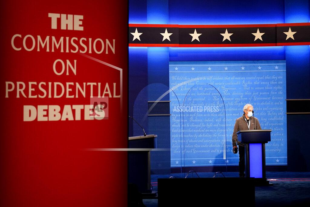 Julio Cortez A member of the production crew stands at a podium near glass barriers to prevent the spread of COVID-19 on stage ahead of the final presidential debate between Republican candidate President Donald Trump and Democratic candidate former Vice President Joe Biden, Wednesday, Oct. 21, 2020, in Nashville, Tenn. The debate will take place Thursday, Oct. 22 at the Curb Event Center at Belmont University. (AP Photo/Julio Cortez)