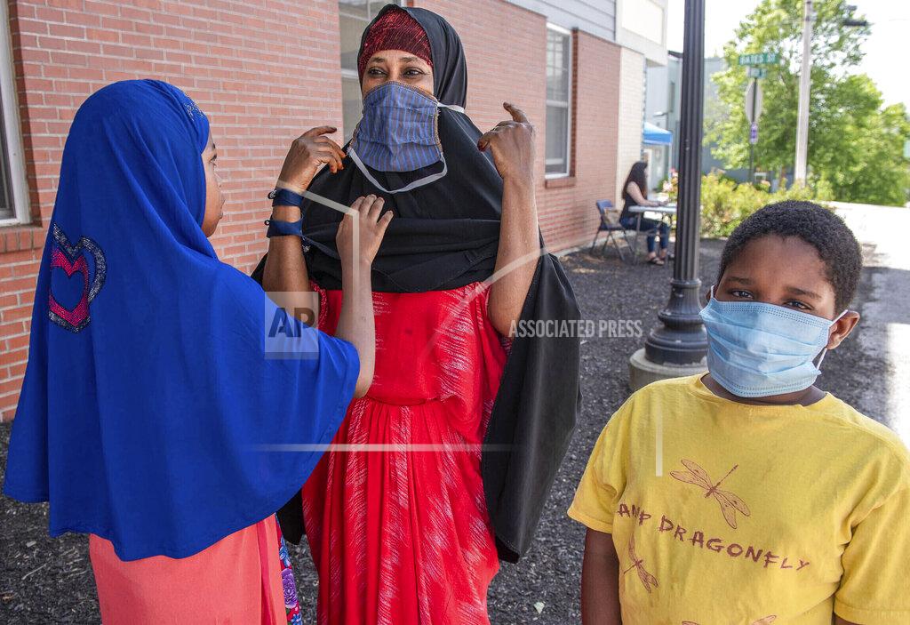 Andree Kehn FILE - In this July 25, 2020, file photo, Asha Dere, center, gets some help putting on her new mask from her daughter Sundus Abdikadir at the B Street Health Center in Lewiston as son Anwar Abdikadir models his new mask. As the world races to find a vaccine and a cure for COVID-19, there is seemingly no antidote in sight to the burgeoning outbreak of coronavirus conspiracy theories, hoaxes, anti-mask myths and sham treatments. (Andree Kehn/Sun Journal via AP, File)