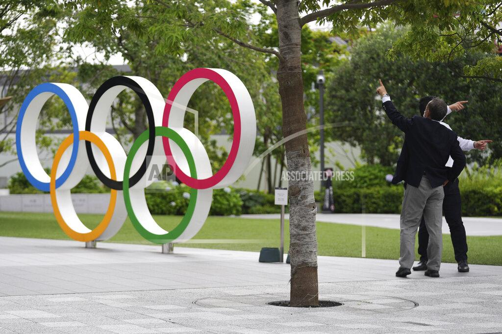 Men gesture near the Olympic Rings Wednesday, June 2, 2021, in Tokyo. (AP Photo/Eugene Hoshiko)