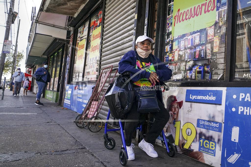 John Minchillo A pedestrian smokes outside a shuttered storefront on Thursday, Oct. 15, 2020, as restrictions are imposed due to a COVID-19 infection increase in the Far Rockaway neighborhood of the borough of Queens in New York. After shutdowns swept entire nations during the first surge of the coronavirus earlier this year, some countries and U.S. states are trying more targeted measures as cases rise again around the world. (AP Photo/John Minchillo)