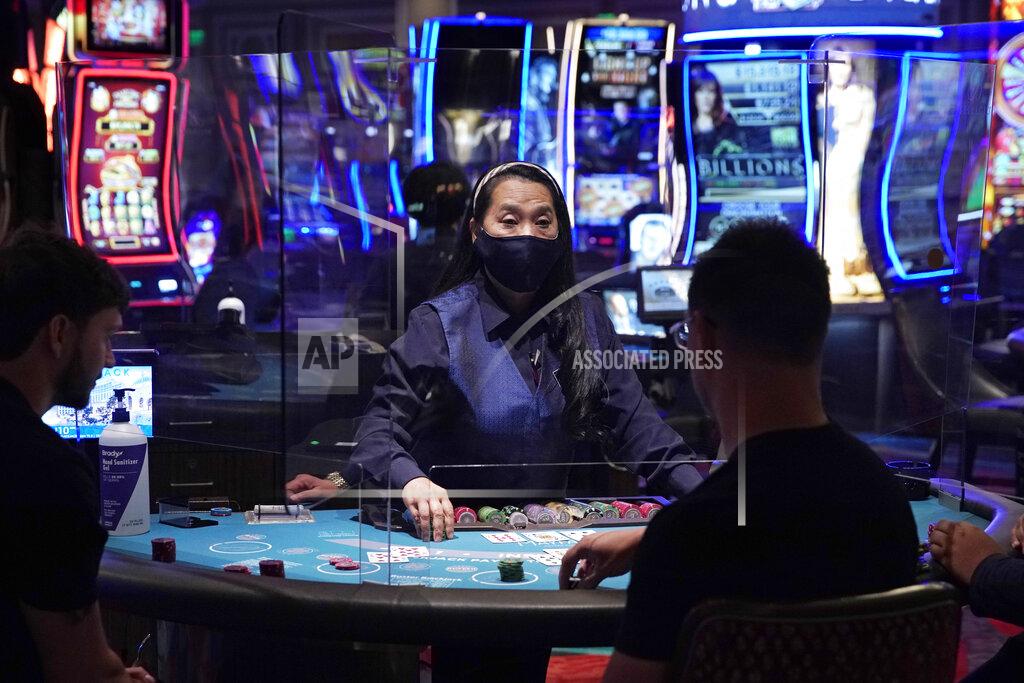 FILE - In this June 4, 2020 file photo, people play blackjack at the reopening of the Bellagio hotel and casino in Las Vegas. Some Las Vegas casinos are updating their smoking policies to limit the practice, which causes people to remove the protective face masks that they're required to wear inside. (AP Photo/John Locher, File)