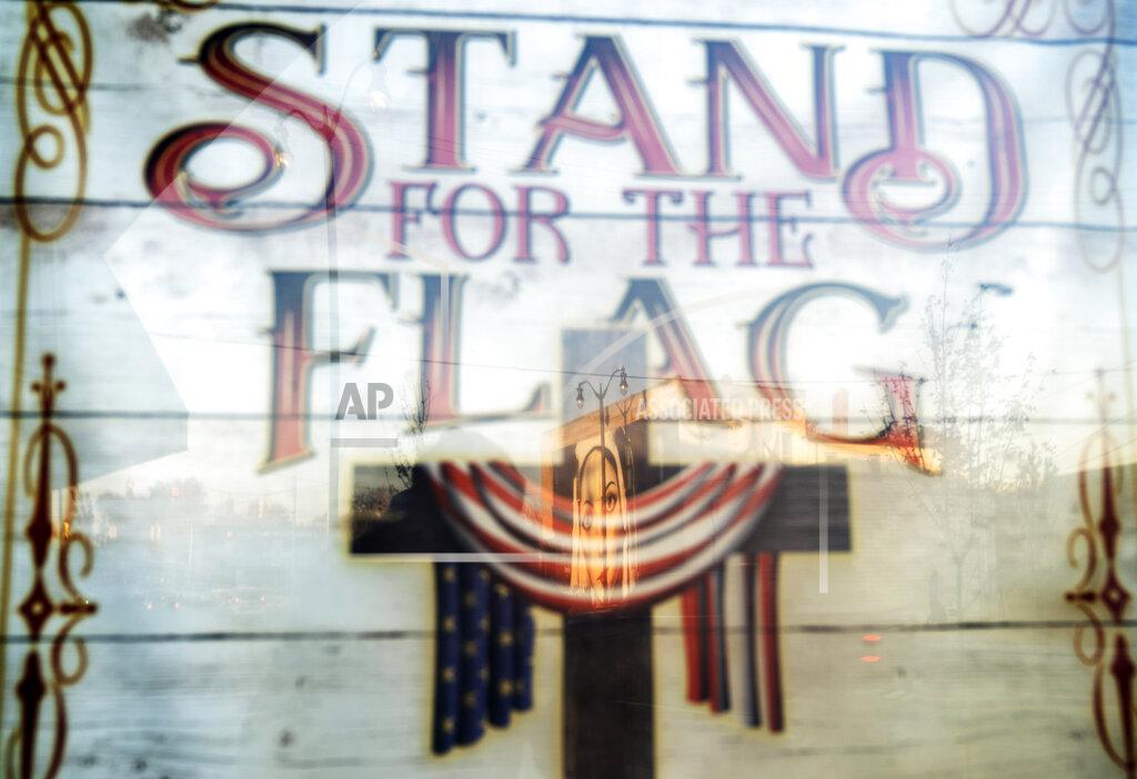 David Goldman A mural of the Virgin Mary, painted on the side of a building, is reflected in a poster which reads "Stand for the Flag, Kneel for the Cross," outside a church in Roseville, Mich., Saturday, Oct. 31, 2020. As the traditional Election Day closes in, Americans are exhausted from constant crises, on edge because of volatile political divisions and anxious about what will happen next. (AP Photo/David Goldman)