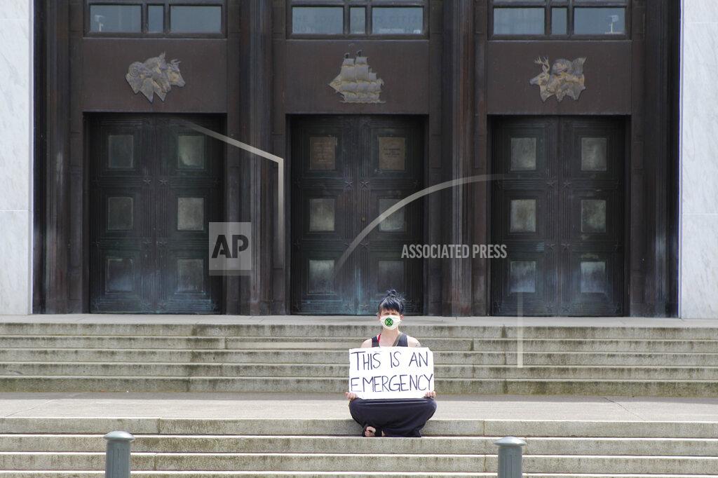 In this Tuesday, June 23, 2020, a lone masked protester sits in front of the Oregon State Capitol in Salem, Ore. Starting Wednesday lawmakers will be meeting in a special session to deal mainly with the coronavirus pandemic and police brutality. (AP Photo/Andrew Selsky)