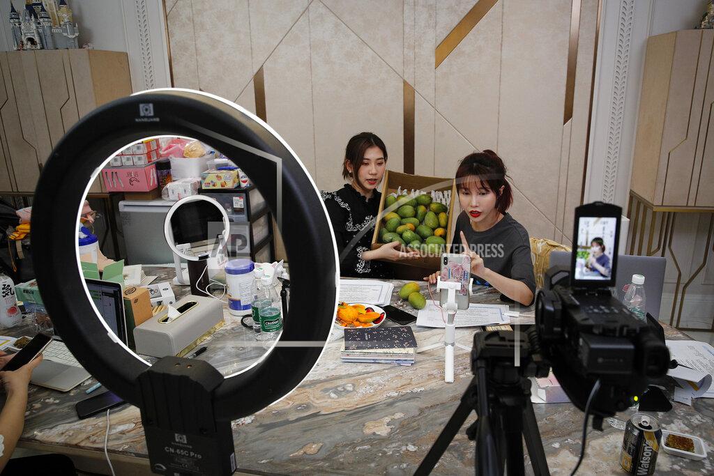 FILE - In this May 5, 2020, photo, China's online celebrity Zhang Mofan, right, introduces fresh mangos to her online clients and fans through the live-streaming at her house in Beijing. Livestream selling, already popular in China, is taking off in the U.S., ushering in a new way for Americans to shop online. Instead of searching for what they want, they pick up their phones, sit back, and click to buy if they like what they see.(AP Photo/Andy Wong)