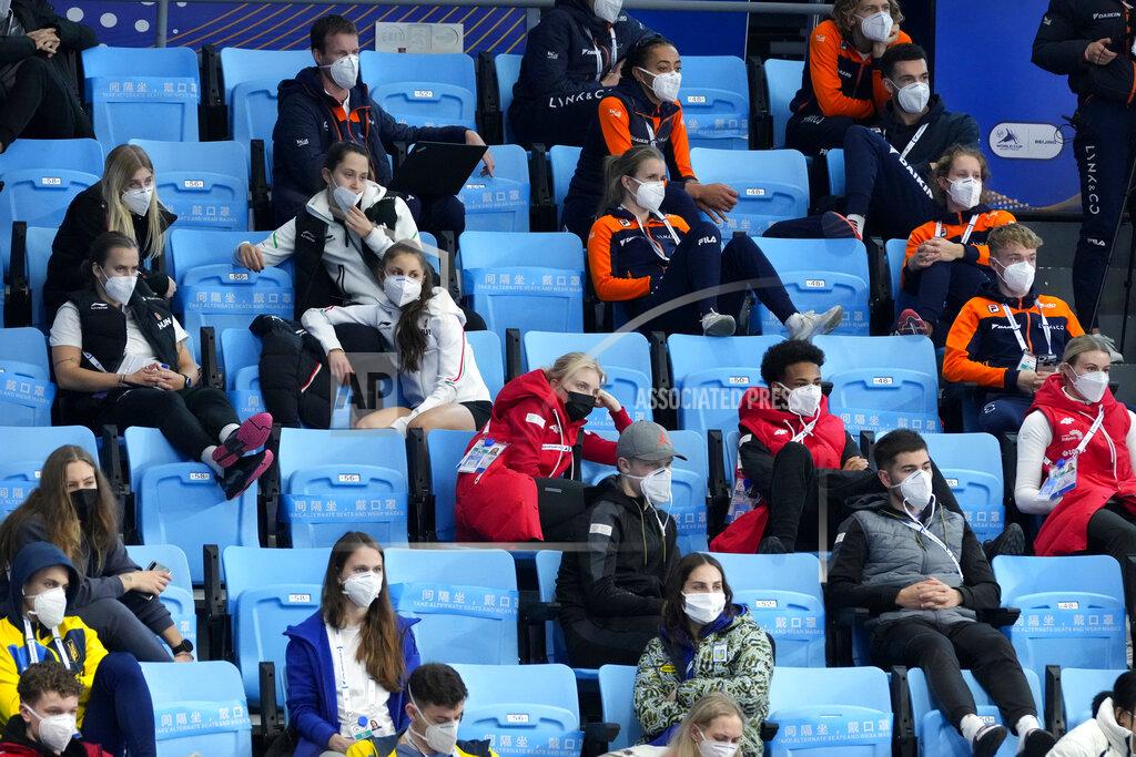 Mark Schiefelbein Athletes wearing face masks to protect against COVID-19 watch the action at the ISU World Cup Short Track speed skating competition, a test event for the 2022 Winter Olympics, at the Capital Indoor Stadium in Beijing, Sunday, Oct. 24, 2021. Already roiled by the pandemic and a partial diplomatic boycott, the Beijing Winter Olympics face another challenge in finding airplane seats for all the athletes and officials. (AP Photo/Mark Schiefelbein)