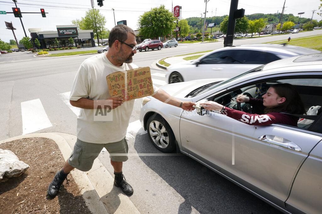 Mark Humphrey Adam Atnip, who is homeless and lives in his car, accepts money from a driver as he panhandles on May 10, 2022, in Cookeville, Tenn. Tennessee is about to become the first U.S. state to make it a felony to camp on local public property such as parks. (AP Photo/Mark Humphrey)