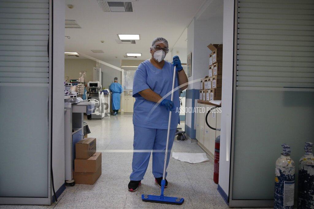 Thanassis Stavrakis Cleaning worker Anthoula Dimitra Pagouni, 30, poses in an ICU entrance of the Sotiria Thoracic Diseases Hospital in Athens, Monday, Jan. 18, 2021. The cleaners of coronavirus intensive care units run a daily gauntlet of infection risks to ensure that ICUs run smoothly, and they are critical to preventing the spread of disease in hospitals. But their status as unskilled laborers in a behind-the-scenes role has left them out of the public eye. (AP Photo/Thanassis Stavrakis)
