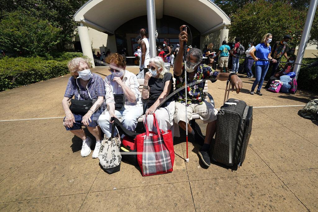 David J. Phillip CORRECTS SPELLING OF FIRST NAME TO ELISABETH INSTEAD OF ELIZABETH - Evacuees, from right to left, Tommie McNeil, Elisabeth Pelham, Nota Norris, and a woman who did not want to be identified, wait to board a bus as they evacuate, Tuesday, Aug. 25, 2020, in Galveston, Texas. The evacuees are being taken to Austin, Texas, as Hurricane Laura heads toward the Gulf Coast. (AP Photo/David J. Phillip)