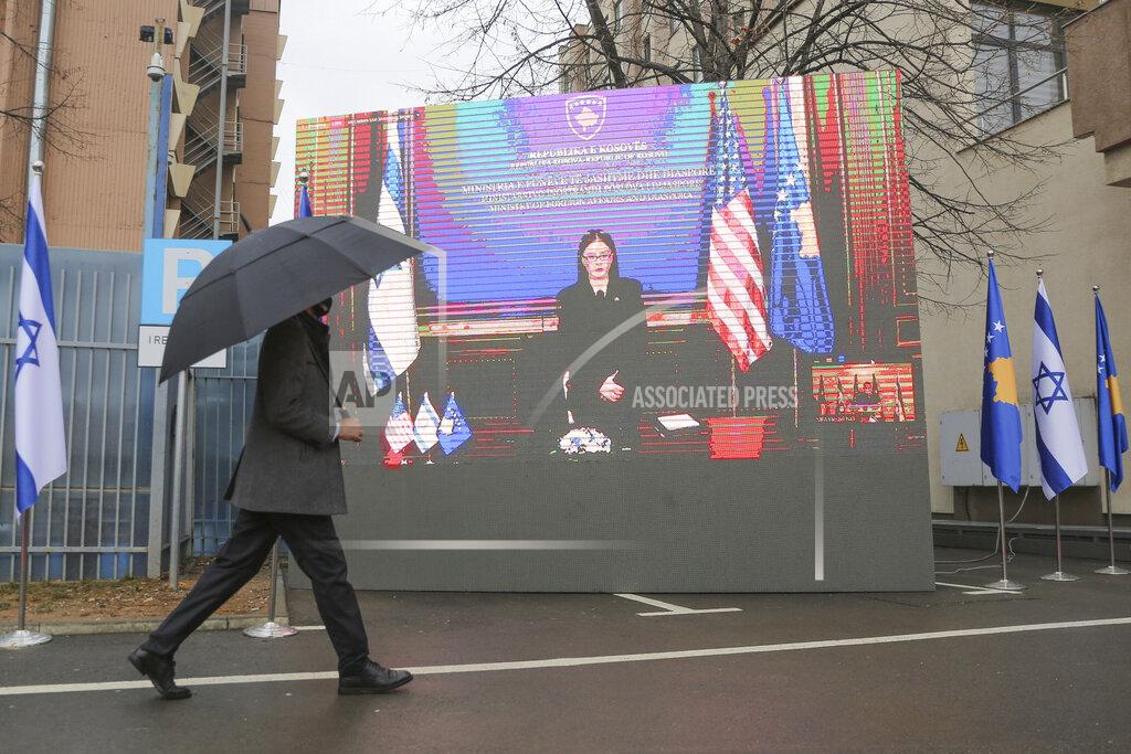 Visar Kryeziu A government official holding an umbrella passes by a monitor displaying Kosovo's Foreign Minister Meliza Haradinaj-Stublla during a signing ceremony held virtually, in the capital Pristina, Monday, Feb. 1, 2021. Kosovo and Israel formally have established diplomatic ties in a ceremony held digitally due to the pandemic lockdown. Kosovo’s Foreign Minister Meliza Haradinaj-Stublla and her Israeli counterpart Gabriel Ashkenazi on Monday held a virtual ceremony signing the documents. The two countries considered it as “making history” and marking “a new chapter.” (AP Photo/Visar Kryeziu)
