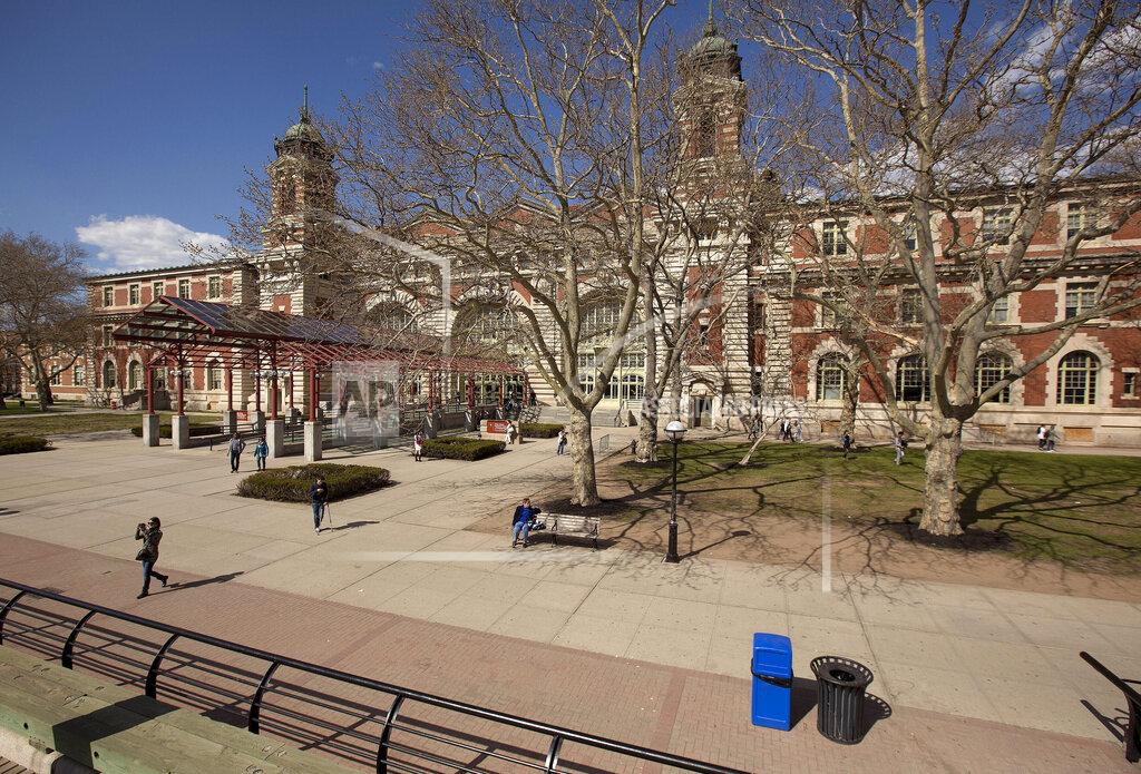 Julie Jacobson FILE - Tourists walk around the grounds at Ellis Island, on April 29, 2015, in New York. The location is featured in a collection of mini-essays by American writers published online by the Frommer's guidebook company about places they believe helped shape and define America. (AP Photo/Julie Jacobson, File)