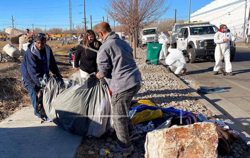Tim Vandenack Residents of a tent city encampment on 33rd Street in Ogden, Utah, move their belongings from the side of the street on Tuesday, Dec. 1, 2020, to make way for Ogden City clean-up crews, seen in white in the background. (Tim Vandenack/Standard-Examiner via AP)