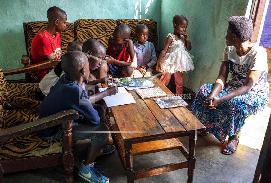 Uncredited Tresor Ndizihiwe, 12, writes in a book accompanied by his siblings and his mother, Jacqueline Mukantwari, right, at their home in Kigali, Rwanda on Tuesday, April 21, 2020 during the COVID-19 coronavirus lockdown. Mukantwari says her son is a good student -- “so intelligent.” (AP Photo)
