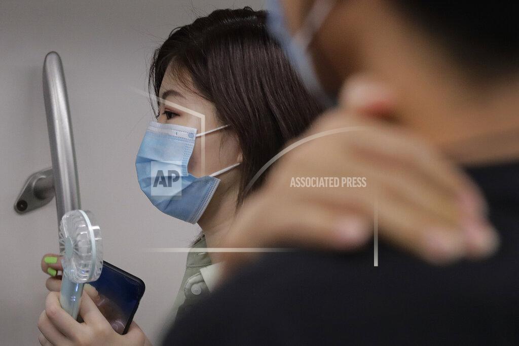 Andy Wong A woman wearing a face mask to protect against the new coronavirus uses an electric fan to cool herself as she rides in a subway train in Beijing, Wednesday, July 29, 2020. China reported more than 100 new cases of COVID-19 on Wednesday as the country continues to battle an outbreak in Xinjiang. (AP Photo/Andy Wong)