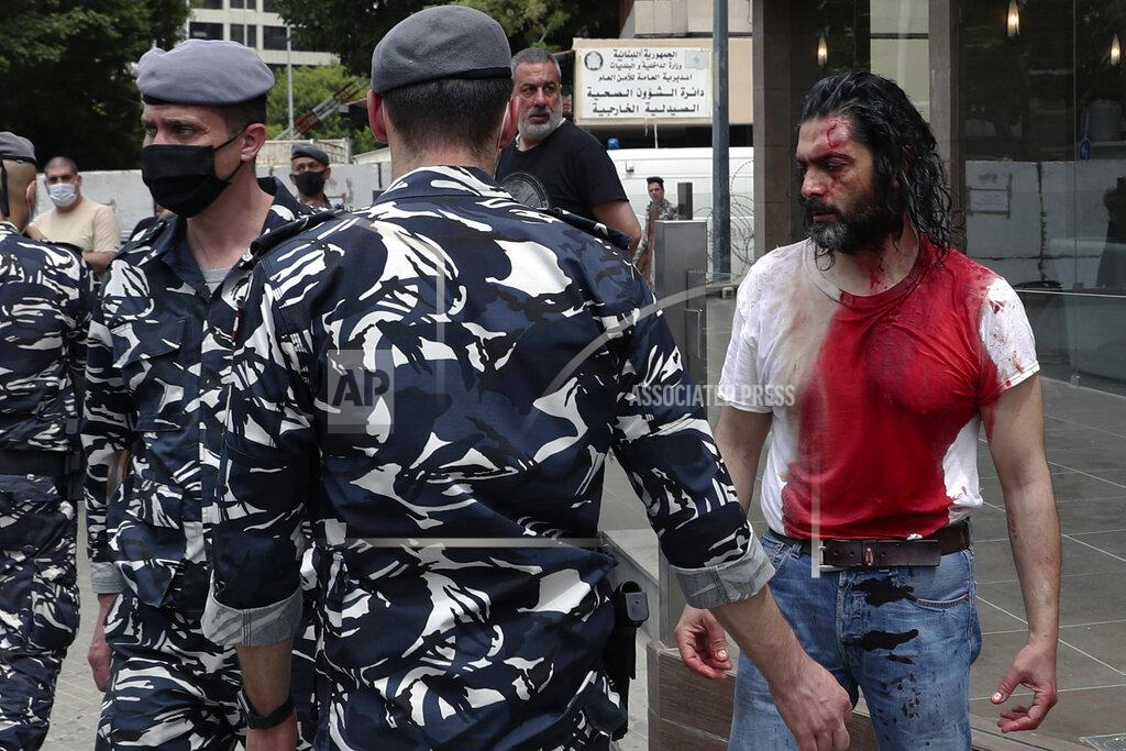 Bilal Hussein FILE - In this April 19, 2021 file photo, policemen stand guard next to a man in a blood-soaked shirt who was viciously beaten by opponents of Judge Ghada Aoun, during a sit-in outside the Justice Palace in Beirut, Lebanon. A public feud in recent weeks among prosecutors has starkly demonstrated how Lebanon's system of sectarian factions is paralyzing Lebanon's judicial system and snarling attempts to root out corruption. Aoun, a prominent prosecutor says she is trying to go after rampant corruption but her critics say she is only targeting enemies of her ally, the president. (AP Photo/Bilal Hussein, File)