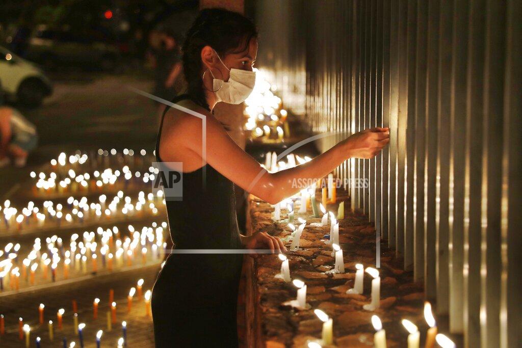 Jorge Saenz Clarisa Gomez lights candles during a vigil in remembrance of those who have died from the COVID-19, in front of the Ministry of Health in Asuncion, Paraguay, Sunday, March 14, 2021. (AP Photo/Jorge Saenz)