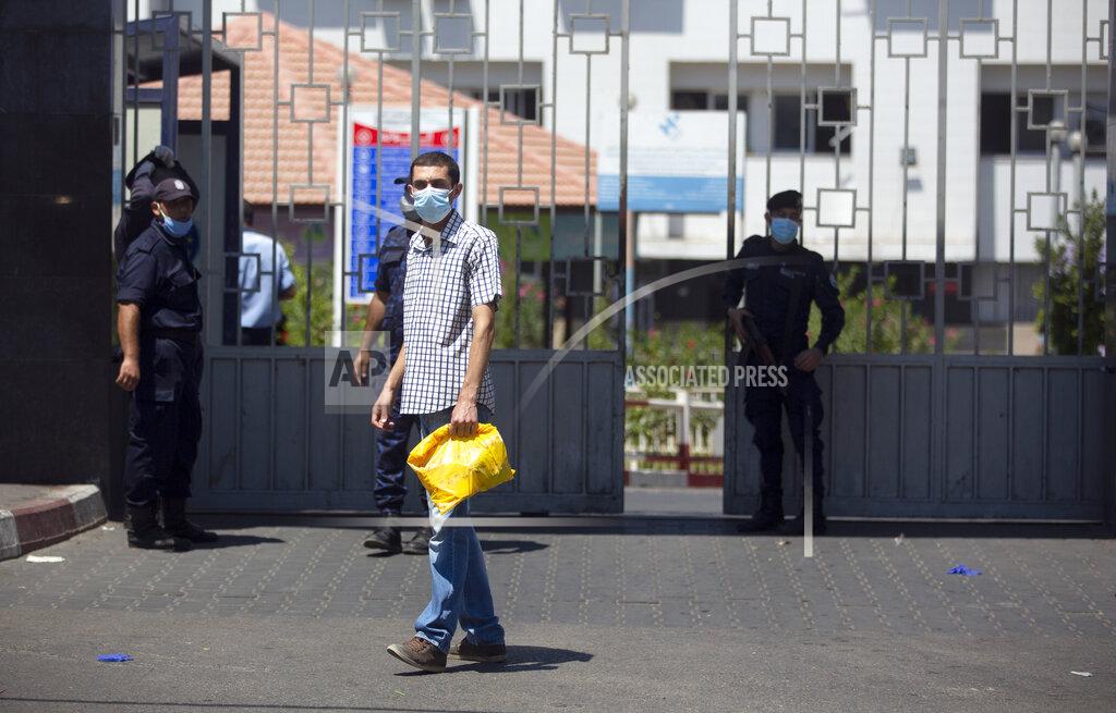 Khalil Hamra CORRECTS THAT HOSPITAL NOT CLOSED -- A Palestinian man wears a face mask as he walks next to Hamas police officers guarding the entrance of the Shifa Hospital where coronavirus cases were discovered, in Gaza City, Wednesday, Aug. 26, 2020. Gaza health officials have reported the first death from COVID-19 since authorities detected community transmission of the coronavirus earlier this week. (AP Photo/Khalil Hamra)