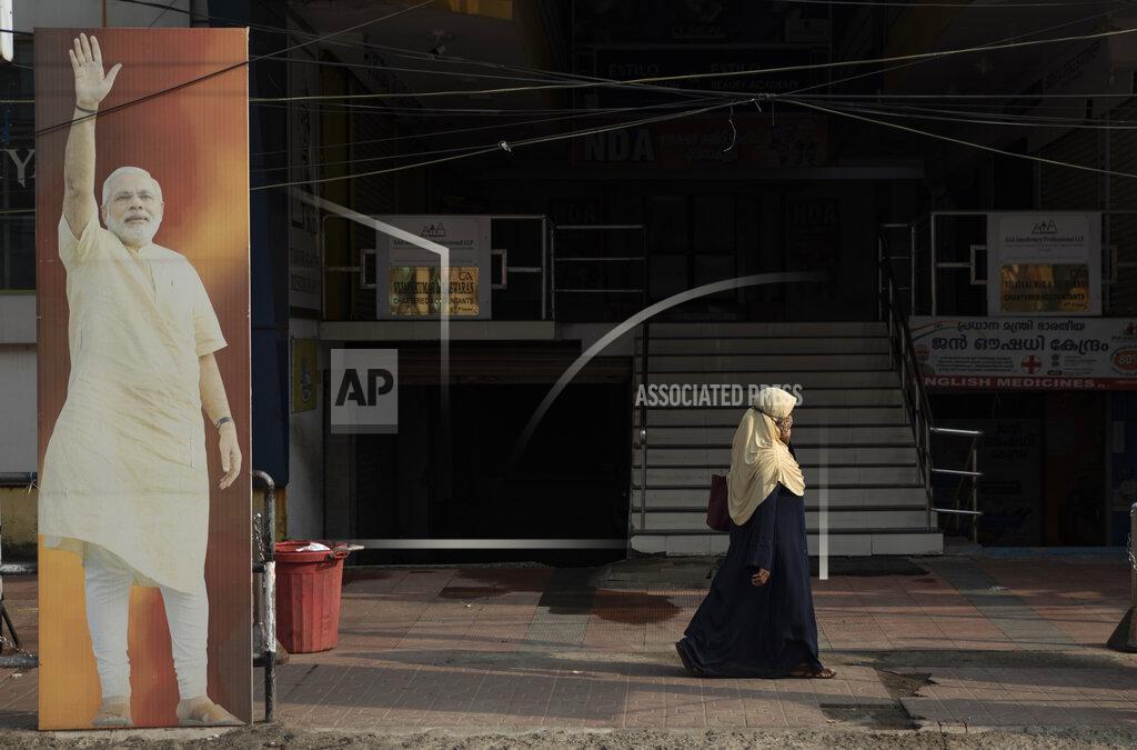 R S Iyer FILE - In this March 26, 2021, file photo, a Muslim woman walks past an image of Prime Minister Narendra Modi displayed outside an office of the Bharatiya Janata Party in Kochi, Kerala state, India. Despite clear signs that India was being swamped by another surge of coronavirus infections, Modi refused to cancel campaign rallies, a major Hindu festival and cricket matches with spectators. The crisis has badly dented Modi’s carefully cultivated image as an able technocrat. (AP Photo/R S Iyer, File)