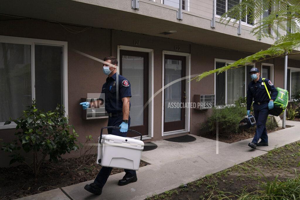 Jae C. Hong Torrance firefighter Trevor Borello, left, carries a cooler containing the Pfizer COVID-19 vaccine as he walks to an apartment to inoculate two sisters who have muscular dystrophy, Wednesday, May 12, 2021, in Torrance, Calif. Teamed up with the Torrance Fire Department, Torrance Memorial Medical Center started inoculating people at home in March, identifying people through a city hotline, county health department, senior centers and doctor's offices, said Mei Tsai, the pharmacist who coordinates the program. (AP Photo/Jae C. Hong)
