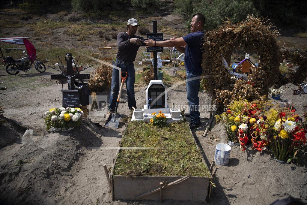 Cemetery worker Jorge Arvizu, left, helps a family member place a plaque on the grave of Vicente Dominguez who died of complications related to the new coronavirus, at the municipal cemetery Valle de Chalco, on the outskirts of Mexico City, Tuesday, Oct. 20, 2020. Mexican families traditionally flock to local cemeteries to honor their dead relatives as part of the “Dia de los Muertos,” or Day of the Dead celebrations, but according to authorities the cemeteries will be closed this year to help curb the spread of COVID-19. (AP Photo/Marco Ugarte)