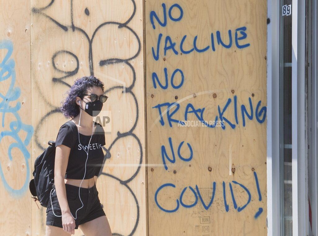 Graham Hughes A woman wears a face mask as she passes by graffiti reading 'No vaccine, No tracking, No COVID', in Montreal, Sunday, Aug. 16, 2020, as the COVID-19 pandemic continues in Canada and around the world. (Graham Hughes/The Canadian Press via AP)